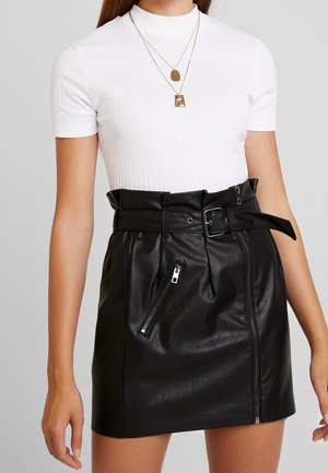 Sort læder mini-nederdel med plisseret design, taljebælte og sidelommer med lynlås, parret med en tætsiddende hvid ribbet top.
