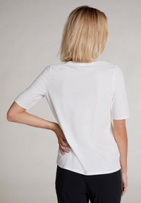 Witte T-shirt met korte mouwen, ronde hals, gladde textuur en een losse pasvorm. Achteraanzicht toont strakke lijnen zonder versieringen.