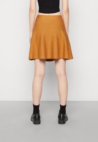 Jupe évasée marron en tissu doux, avec une texture lisse et une longueur mi-cuisse, associée à des chaussettes noires et des chaussures.