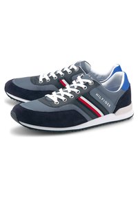 Paire de baskets basses bleu marine et grises avec des lacets blancs, des accents bleus au talon, et des détails rayés rouge, blanc et bleu sur les côtés.