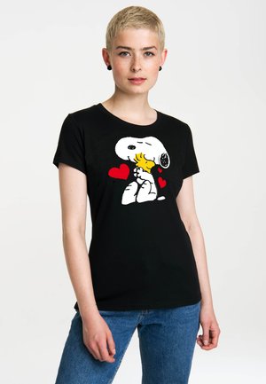 Young person with short blonde hair wearing a black t-shirt featuring Snoopy hugging Woodstock with three red hearts.