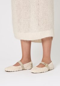 Ballerine color crema con una consistenza soffice, punta arrotondata e una cinghia beige alla caviglia con un accento di fibbia dorata.