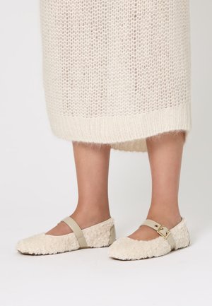 Ballerine color crema con una consistenza soffice, punta arrotondata e una cinghia beige alla caviglia con un accento di fibbia dorata.