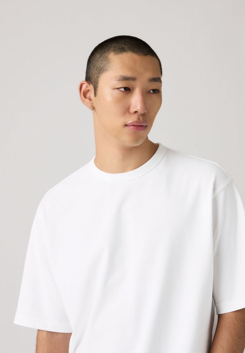 T-shirt blanc en coton avec une coupe décontractée, manches courtes et encolure ronde. Texture lisse sans motifs ni accents visibles.