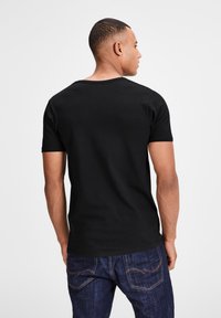 Schwarzes T-Shirt mit kurzen Ärmeln aus Baumwolle, mit rundem Halsausschnitt und taillierter Passform, kombiniert mit blauen Denim-Jeans.