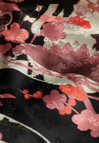 Tessuto di seta con sfondo nero, caratterizzato da intricati motivi floreali in tonalità di rosa e rosso, insieme a dettagli testurizzati e finiture delicate.
