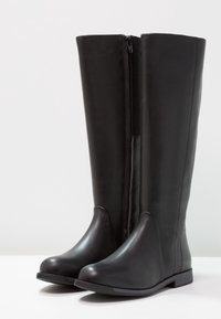 Botas negras hasta la rodilla hechas de cuero suave, con punta redonda, cremallera lateral y un ligero tacón. Presentan un diseño elegante y minimalista.