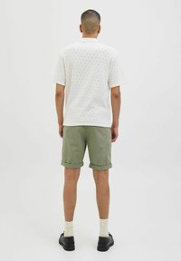 White short-sleeve shirt with a textured pattern, paired with olive green rolled-up shorts, white socks, and black shoes.