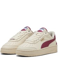 Cream-colored sneakers with a maroon stripe and accents. Features perforated tip, flat laces, and a textured rubber sole. Brand logo on tongue.