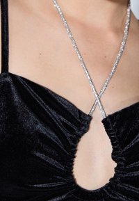 Czarna aksamitna bluzka z marszczeniem i dekoltem w kształcie łezki. Posiada krzyżujące się paski z błyszczącym srebrnym akcentem w postaci łańcuszka.