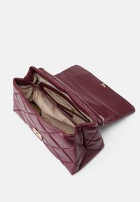 Quilted bordeaux vegansk læder håndtaske med guld hardware, der har to indvendige rum og en låseclip. Glat indvendig foering.