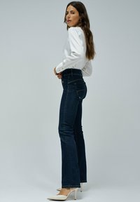 Jeans acampanados de color azul oscuro combinados con una blusa blanca. Los jeans tienen una cintura alta y cuentan con bolsillos traseros clásicos.