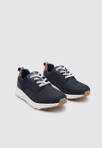 Zapatillas azul marino con parte superior de malla, cordones blancos y suela beige. Presenta detalles en marrón claro en el talón y un diseño de punta redondeada.