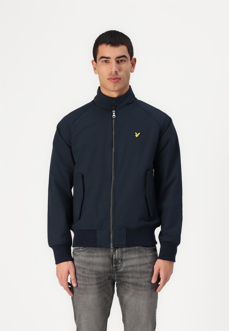 Giacca zip-up blu marina con colletto alto, due tasche laterali e un piccolo logo giallo sul petto. Tessuto liscio e design attillato.