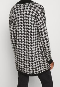 Zwart-wit houndstooth patroon cardigan gemaakt van breiwerk, met een ronde halslijn en geribde manchetten, en een langere achterzoom.
