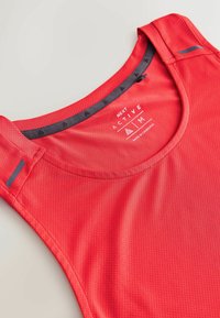 Haut de sport sans manches rouge avec tissu en maille évacuant l'humidité, encolure ronde et détails réfléchissants sur les bretelles.