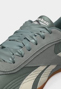 Κοντινό πλάνο γκρι αθλητικού παπουτσιού Reebok με γκρι σατέν κορδόνια, υφές από σουέντ και δέρμα, και σόλα από καουτσούκ ορατή στην κάτω άκρη.