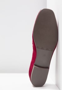 Semelle d'une chaussure plate en daim rouge vue de face, taille 37 estampillée sur la semelle lisse marron et talon carré bas sur fond blanc.