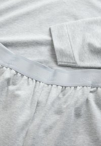 Gray cotton pajamas featuring a relaxed fit, elastic waistband with "NEXT SIGNATURE" embossed, and a soft texture.