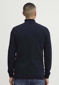 Marineblauer Strickpullover mit hohem Kragen, langen Ärmeln und gerippten Bündchen und Saum. Glatte Textur, taillierte Passform, keine sichtbaren Muster oder metallischen Elemente.