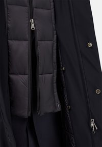 Abrigo negro con interior acolchado, cremalleras dobles y botones a presión; textura suave con secciones acolchadas y un corte entallado.