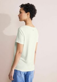Light green short-sleeve t-shirt with a relaxed fit, featuring a rounded neckline and a small logo detail near the shoulder on the back.