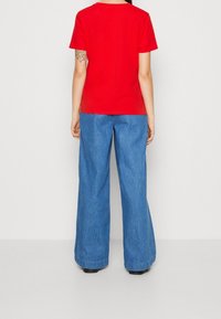 Rød kortærmet t-shirt kombineret med løse, højtaljede blå denim bukser. T-shirten har en rund halsudskæring, og bukserne er glimrende forneden.