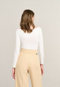 White long-sleeve top with an off-shoulder design, paired with high-waisted beige wide-leg pants. Smooth texture, subtle sheen.