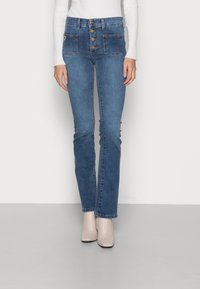 Högmidjade, blå denimjeans med femknapps-gylf, två framfickor och lätt blekning, ihop med beiga ankelstövlar.