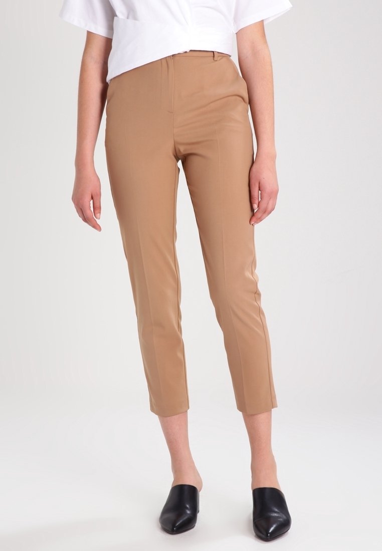 Pantalon beige ajusté, coupe slim, longueur cheville, en tissu lisse. Assorti à des mules noires ouvertes à l'avant et un haut court blanc.