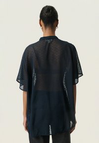 Camicia navy a vestibilità ampia con un design testurizzato e trasparente e motivo a pois, caratterizzata da maniche corte e colletto. Dettaglio hardware discreto sulla schiena.