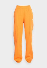 Nike-joggingbyxor i varm orange, med elastiskt midjeband, muddar vid anklarna och en liten vit logotyp på vänster sida. Slät tygtextur.