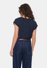 Tumši zils īsām piedurknēm krekls ar sarullētām oderēm, apvienots ar augsto vidukli tumšas denima džinsiem, kuros ir brūnas ādas jostas un aizmugures kabatas.