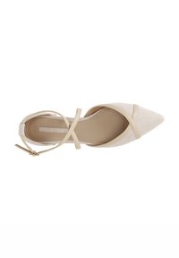 Zapato beige de punta afilada con un exterior texturizado, correas en forma de cruz en el tobillo y una suela lisa. El diseño presenta un hardware mínimo y un acabado limpio.