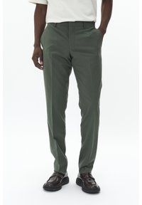 Pantalons vert olive à coupe ajustée, dotés de poches latérales et d'une texture lisse, associés à des chaussures marron foncé.