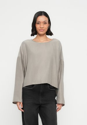 Haut gris clair à manches longues raccourcies avec un col large et une coupe décontractée, associé à un pantalon en denim noir taille haute. Texture lisse.