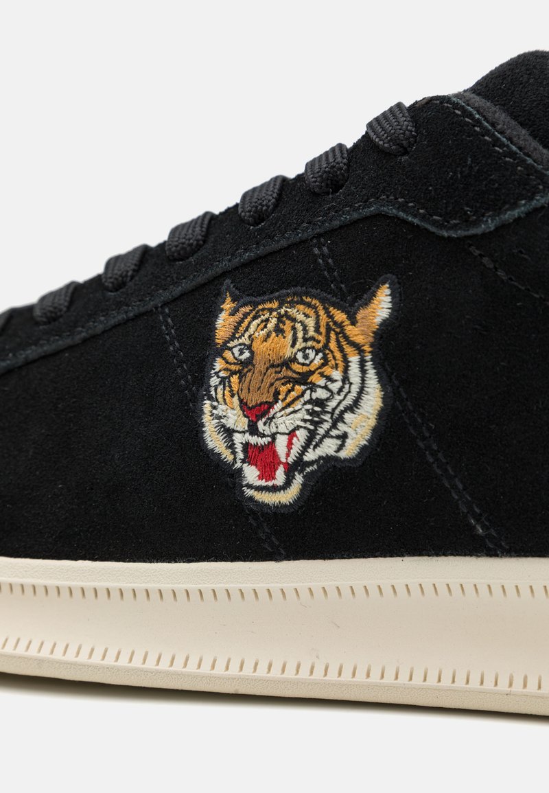 Schwarze Wildleder-Sneaker mit einem detaillierten gestickten Tigerdesign. Weiße Gummisohle mit strukturiertem Nähen. Schwarze Schnürsenkel runden den Look ab.