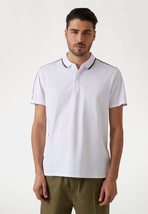 Camisa polo blanca con cuello y tres botones, con ribetes negros en el cuello y los hombros, hecha de una tela suave.