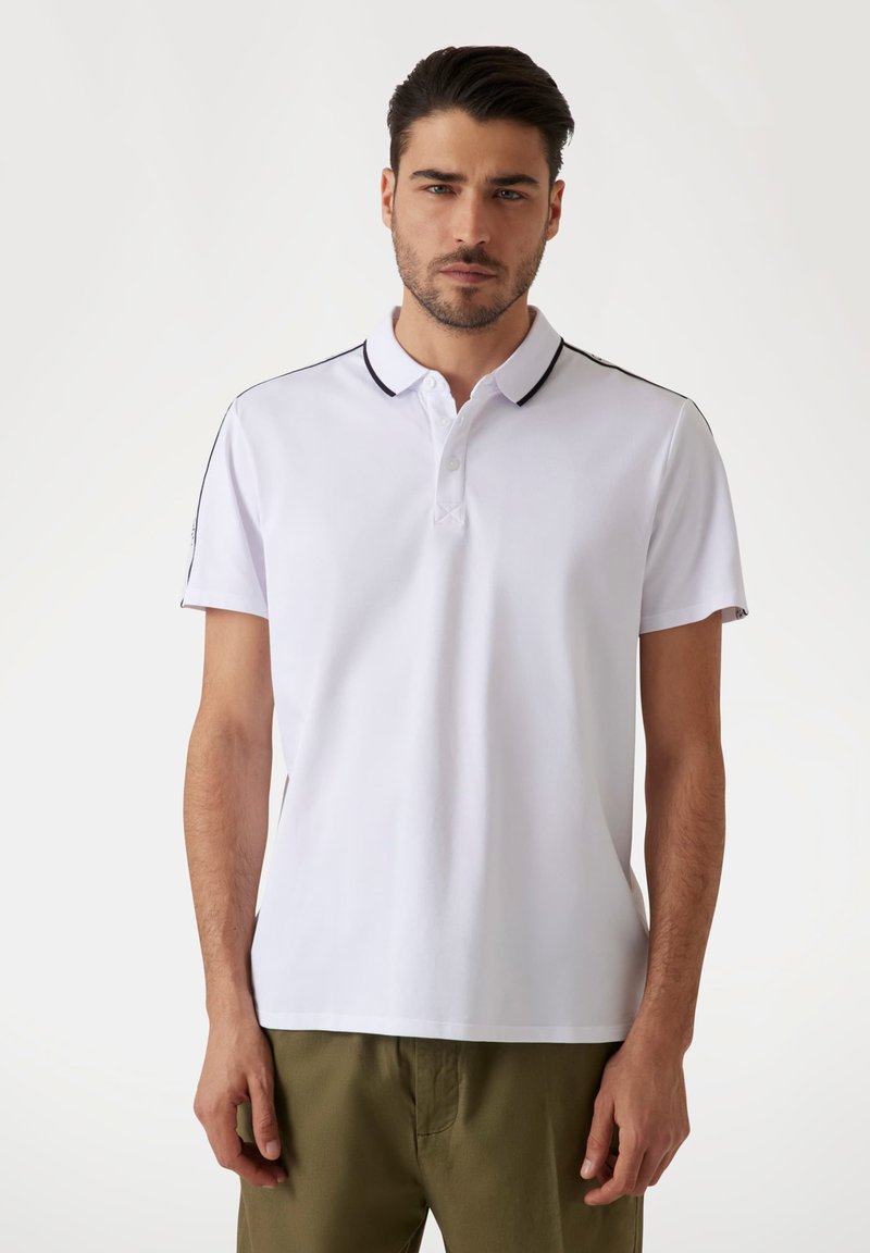 Camisa polo blanca con cuello y tres botones, con ribetes negros en el cuello y los hombros, hecha de una tela suave.