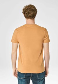 T-shirt a maniche corte di colore arancione chiaro con scollatura rotonda, realizzata in cotone soffice, mostrata da dietro con un design semplice.