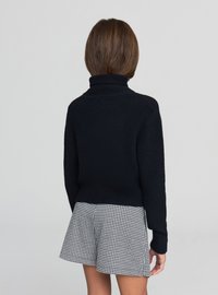 Maglione nero con collo alto, orlo a costine e trama lavorata. Indossato con pantaloncini a scacchi, per un look casual a strati.