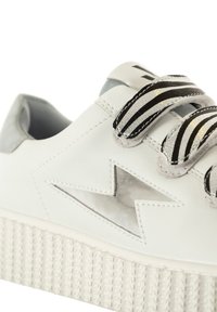 Baskets en cuir blanches avec une semelle texturée, des lacets noirs et argentés rayés, et un design distinctif d'étoile découpée sur le côté.