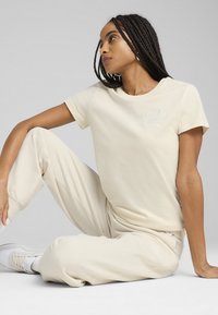 Lichtbeige katoenen t-shirt met korte mouwen en geborduurd "Puma" logo, gecombineerd met bijpassende beige joggers. Zachte textuur.