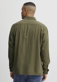 Olijfgroen overhemd met lange mouwen en een comfortabele pasvorm, met knopenmanchetten en een zachte stofstructuur, gecombineerd met blauwe denim jeans.