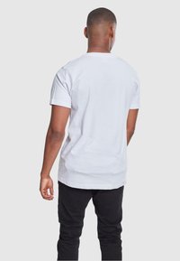 Witte katoenen T-shirt met korte mouwen, ronde hals, normale pasvorm, gladde textuur, eenvoudige achterkant, gecombineerd met zwarte broek.