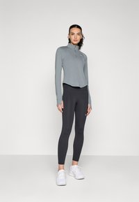 Lysegrå langermet topp med halvmansjett, kombinert med svarte leggings. Begge er laget av elastisk stoff og har et enkelt design.