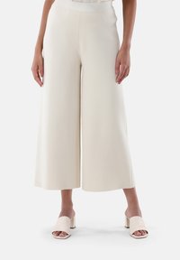 Weiße, weit geschnittene Hosen aus einem weichen Stoff mit glatter Textur, ausgestattet mit einem mittelhohen Bund und seitlichen Taschen. Kombiniert mit hellrosa Blockabsatz-Mules.