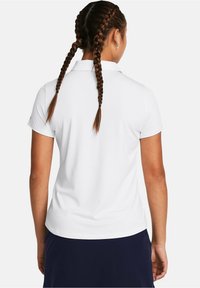 Biała koszulka polo z krótkimi rękawami, gładka w dotyku, standardowy kołnierzyk i proste wykończenie, noszona z granatową spódnicą. Włosy ułożone w dwa warkocze.