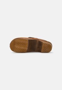 Semelle en caoutchouc brun avec un motif en zigzag, textures contrastées et accents en bois. Légère usure sur le talon, forme arrondie et conception au profil bas.