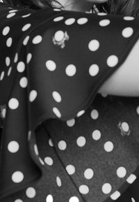 Mustaa kangasta, jossa on suuria valkoisia pilkkuja, sisältäen virtaavan muodon ja kaarevat reunat. Sisältää teksturoitua pintaa ja hienovaraisia yksityiskohtia.